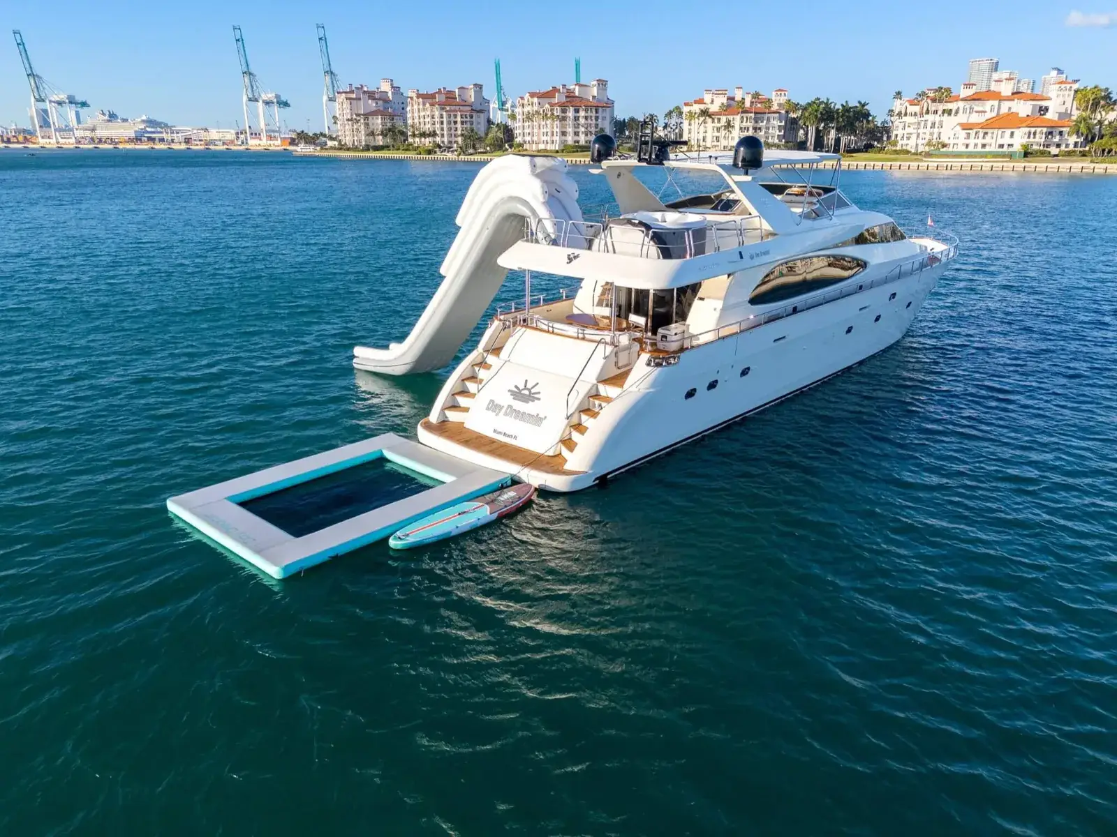 Phygital Group A large white yacht with a waterslide, pool, and paddleboard floats on calm blue water near a city shoreline. Full Service Marketing Agency
